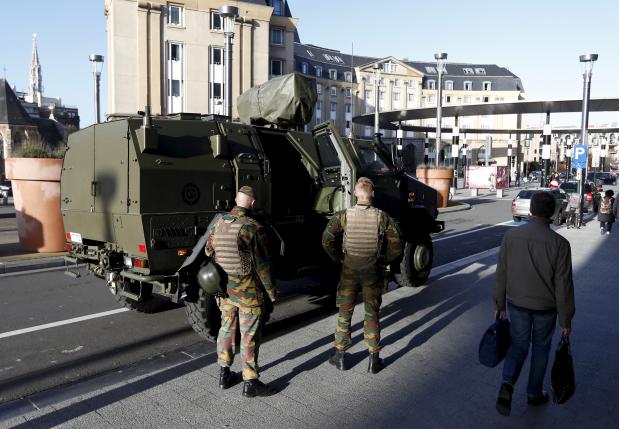 Belgian soldiers stand next to a military armoured vehicle as they patrol in central Brussels