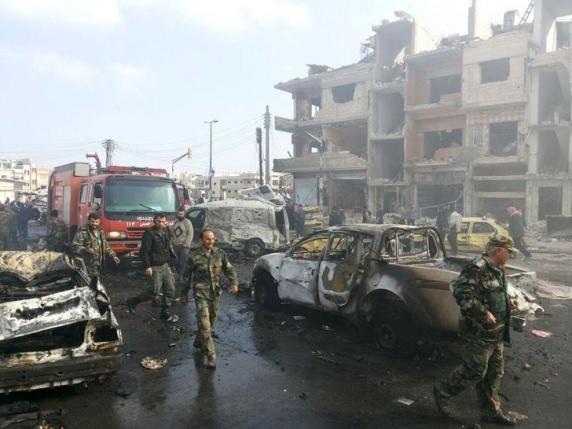 Syrian army soldiers inspect the site of a two bomb blasts in the government-controlled city of Homs