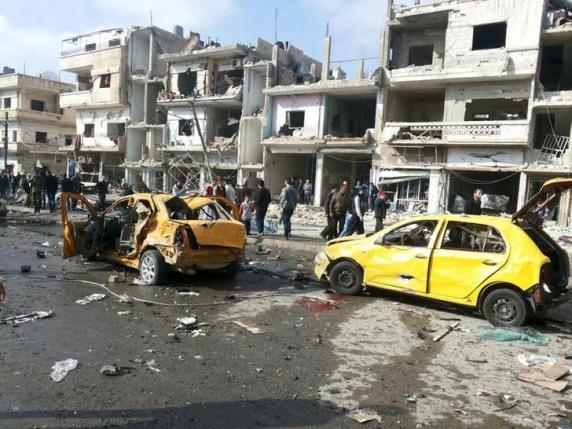 Syrian army soldiers and civilians inspect the site of a two bomb blasts in the government-controlled city of Homs