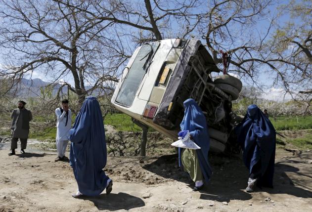 Women walk past a damaged mini-bus after it was hit by a bomb blast in the Bagrami district of Kabul, Afghanistan