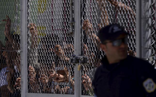 Migrants and refugees stand behind a fence as Pope Francis visits at the Moria refugee camp near the port of Mytilene, on the Greek island of Lesbos