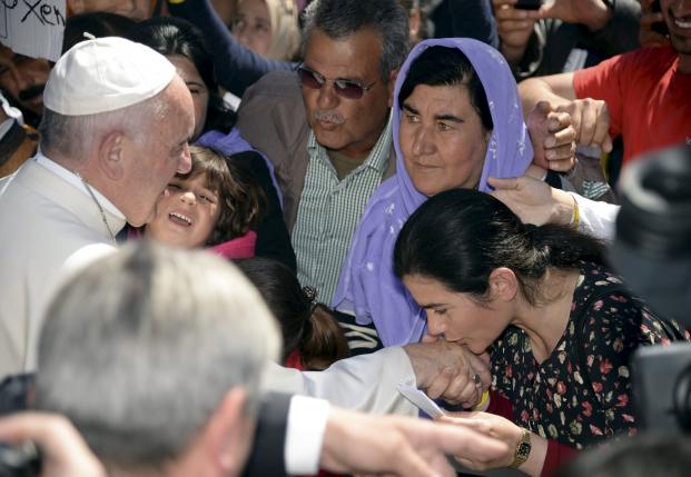 A woman shakes the hand of Pope Francis and gives him a piece of paper as he greets migrants and refugees at the Moria refugee camp near the port of Mytilene, on the Greek island of Lesbos