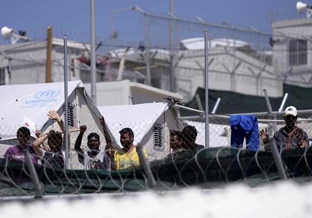 Migrants and refugees stand behind a fence as Pope Francis visits at the Moria refugee camp near the port of Mytilene, on the Greek island of Lesbos