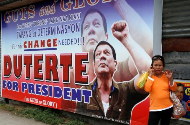 A resident talks on her mobile phone beside a huge election campaign poster of leading presidential candidate Duterte in Davao city