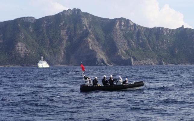 A Japan Coast Guard boat and vessel sail as one of the disputed islands is pictured in the background, in the East China Sea