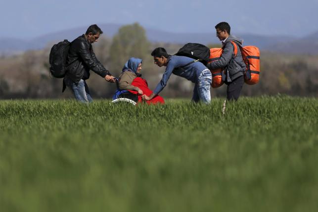 Migrants push a woman in a wheelchair as they walk through a field towards a makeshift camp at the Greek-Macedonian border, near the village of Idomeni