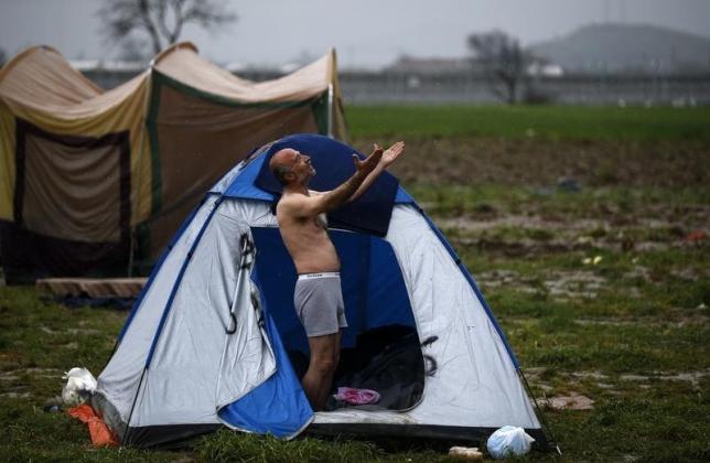 A migrant, who is waiting to cross the Greek-Macedonian border, reacts while being photographed at a makeshift camp near the village of Idomeni