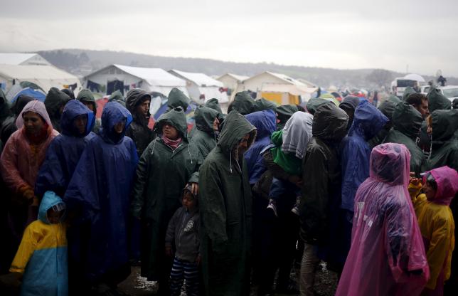 Migrants line up for food during a heavy rainfall at a makeshift camp on the Greek-Macedonian border, near the village of Idomeni