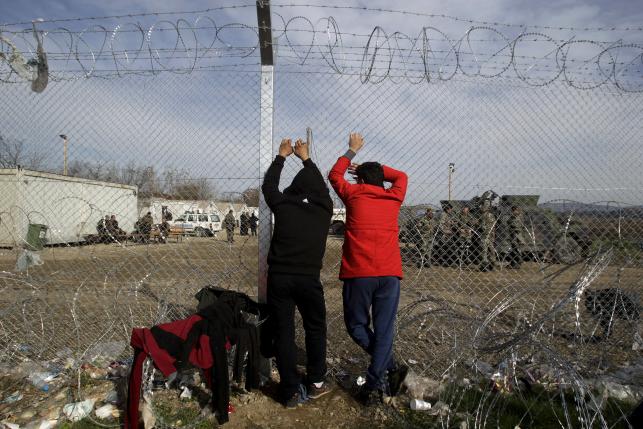 Two migrants look through a border fence towards the Macedonian side of the border, near the village of Idomeni