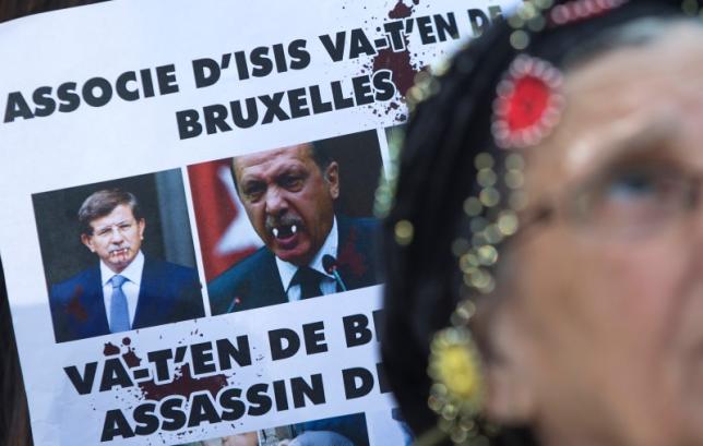 A Kurdish woman displays a defaced picture of Turkish Prime Minister Ahmet Davutoglu and  Turkish President Tayyip Erdogan during a protest outside an EU leaders summit addressing the influx of refugees and migrants flowing into Europe, in Brussels
