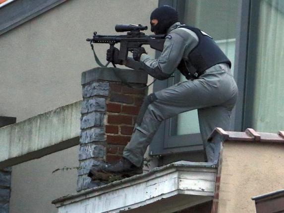 A masked Belgian policeman secures the area from a rooftop near the scene where shots were fired during a police search of a house in the suburb of Forest near Brussels