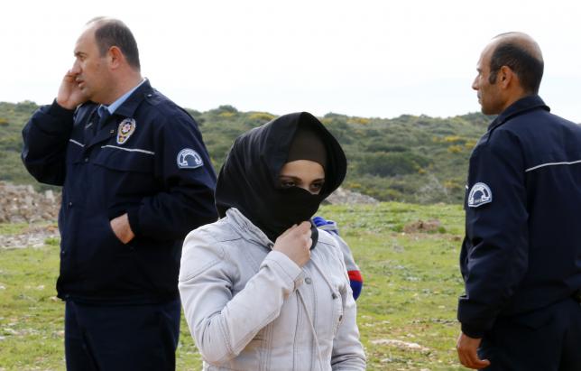 A Syrian refugee woman stands by policemen on a roadside after being prevented from sailing off to the Greek island of Farmakonisi by dinghies, near a beach in the western Turkish coastal town of Didim