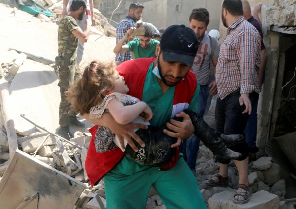 A civil defence member carries a child that survived from under the rubble at a site hit by airstrikes in the rebel held area of Old Aleppo