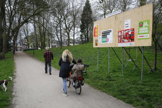 People walk past a billboard with posters about the consultative referendum on the association between Ukraine and the European Union in a park in Utrecht
