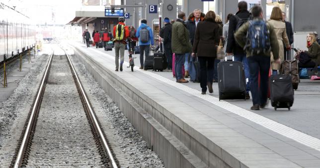 People wait for a train on a platform of the main train station in Munich