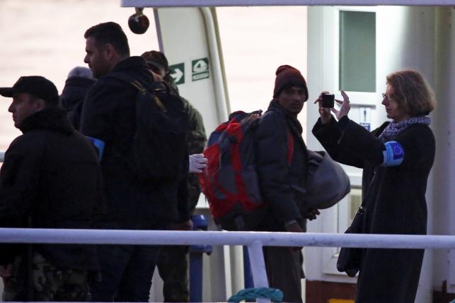 A Frontex officer takes a picture as migrants board a Turkish-flagged passenger boat to be returned to Turkey, on the Greek island of Lesbos