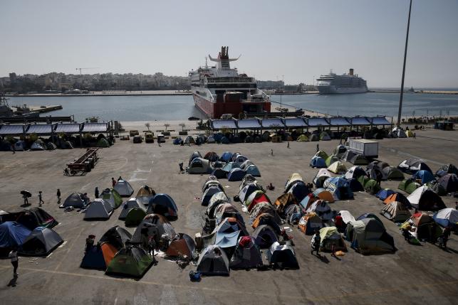 Refugees and migrants make their way next to tents at a makeshift camp at the port of Piraeus, near Athens