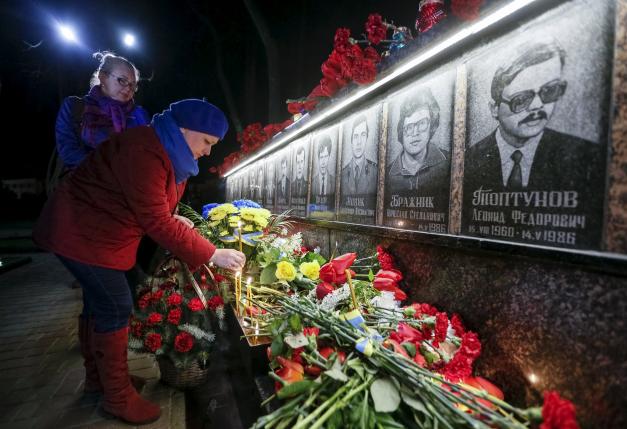 A woman lays flowers at a memorial, dedicated to firefighters and workers who died after the Chernobyl nuclear disaster, during a night service in the city of Slavutych