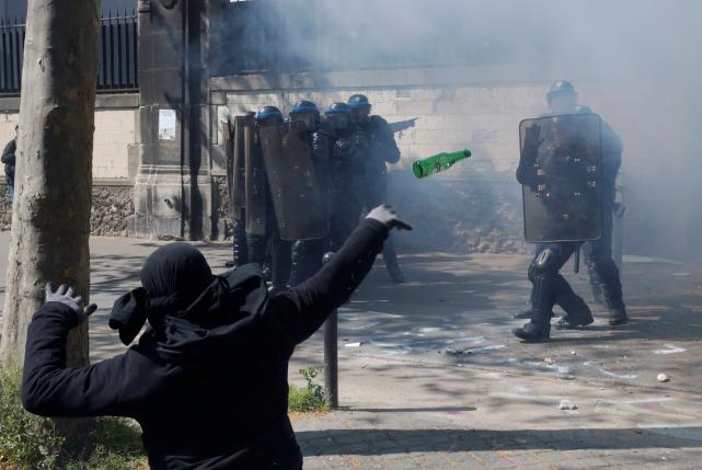 A hooded youth throws a bottle during a clash with French riot police to protest against the French labour law proposal during the May Day labour union march in Paris