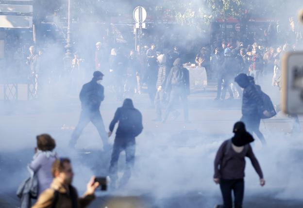 Masked and hooded youths run through clouds of tear gas at the Place de la Nation   as French CRS riot police advance at the end of a protest against the French labour law proposal during the May Day labour union march in Paris