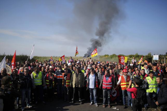 Striking French CGT labour union employees stand near a burning barricade before a police operation to free up a fuel depot near the Donges oil refinery