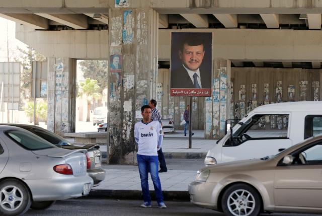 People walk past a poster of Jordan's King Abdullah near the General Intelligence directorate offices near al Baqaa Refugee Camp