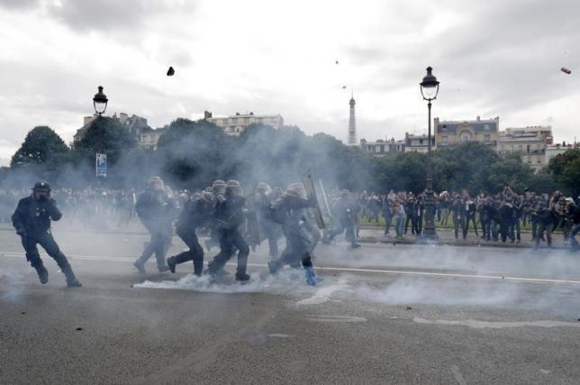 French CRS riot police protect themselves from flying debris during clashes with demonstrators at the Invalides square during a demonstration in Paris